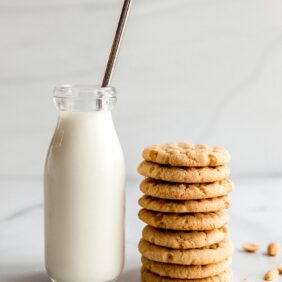 glass bottle of milk with metal straw next to stack of peanut butter cookies