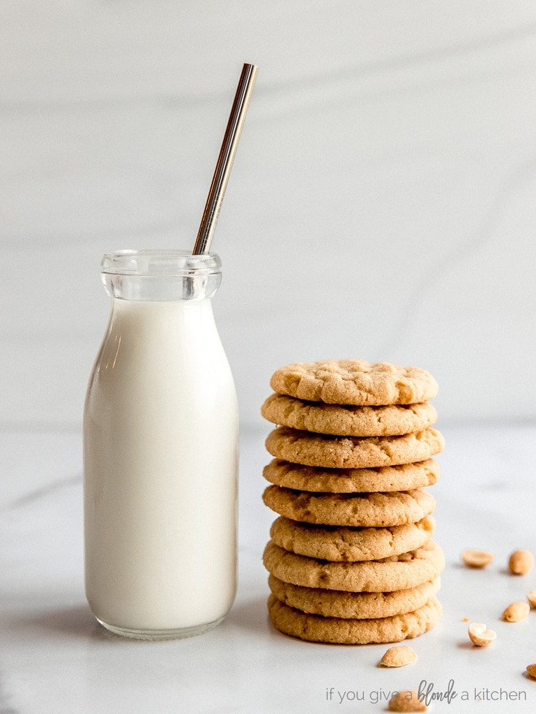 glass bottle of milk with metal straw next to stack of peanut butter cookies