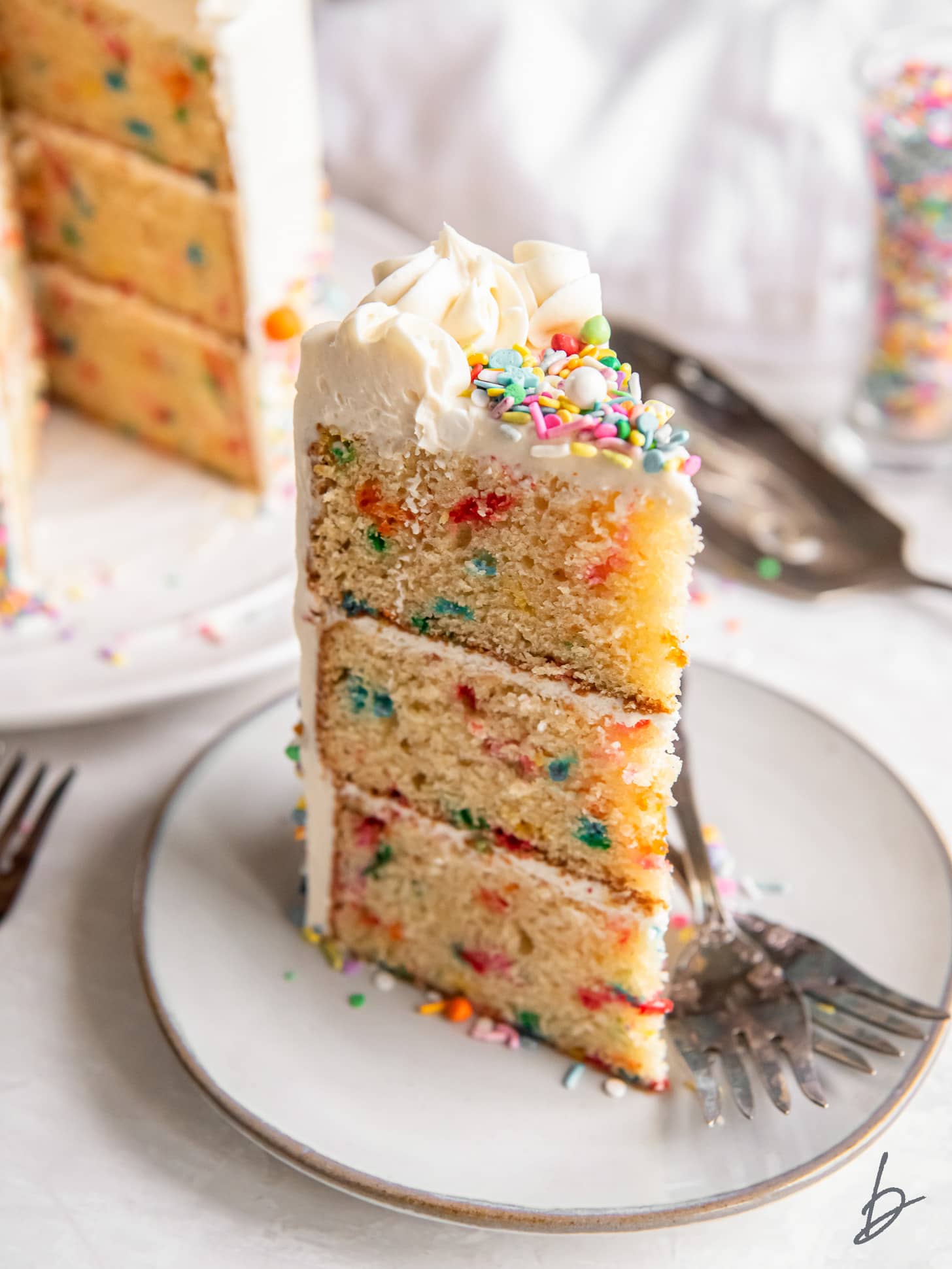 slice of layered funfetti cake on plate with two forks.
