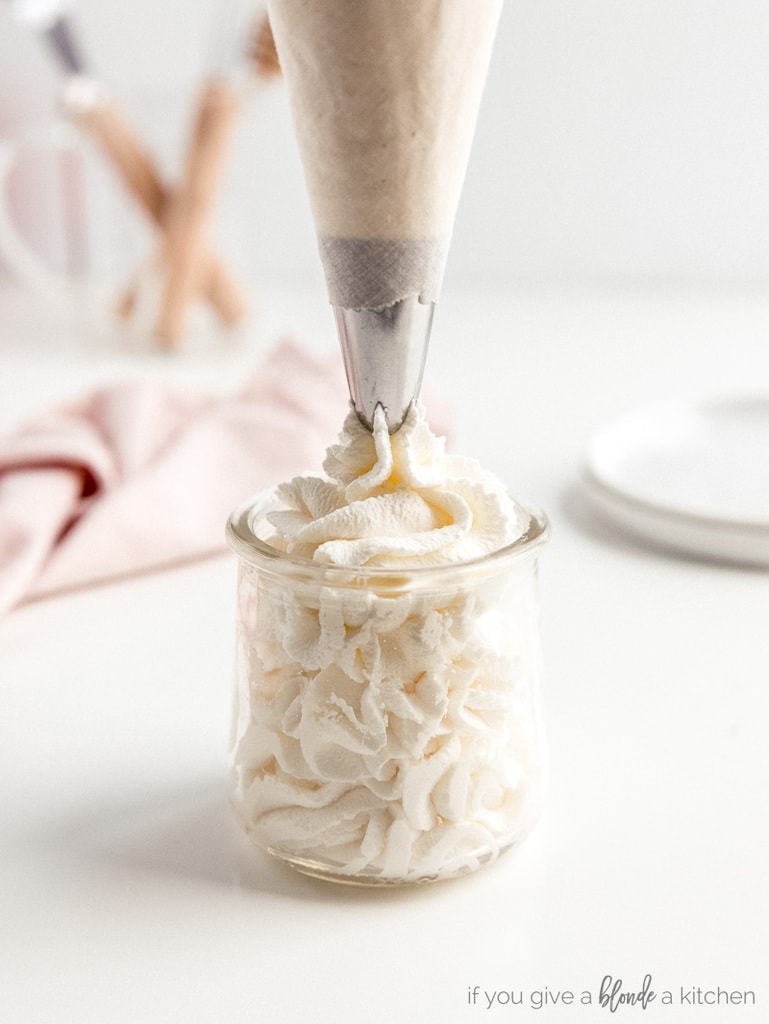 piping bag with tip filling glass jar with homemade whipped cream