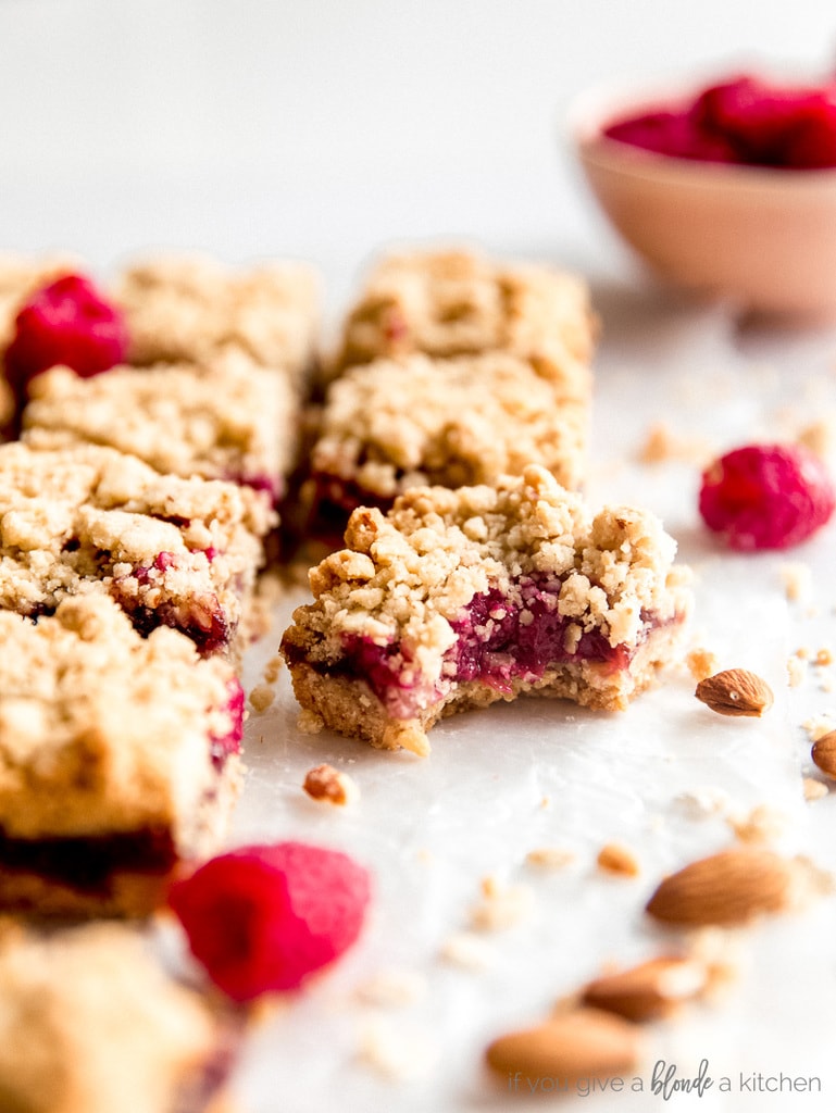 raspberry oatmeal bar with bite. next to more bars and fresh raspberries