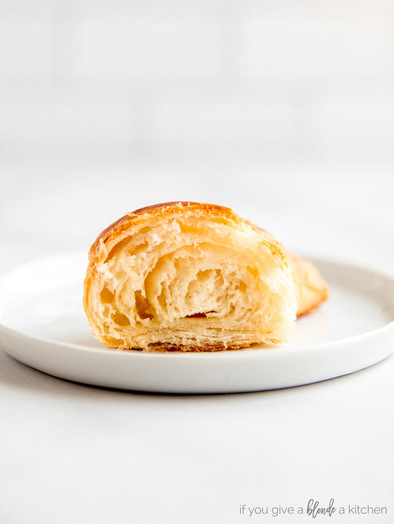 half a croissant on white round plate. Cut to show layers inside