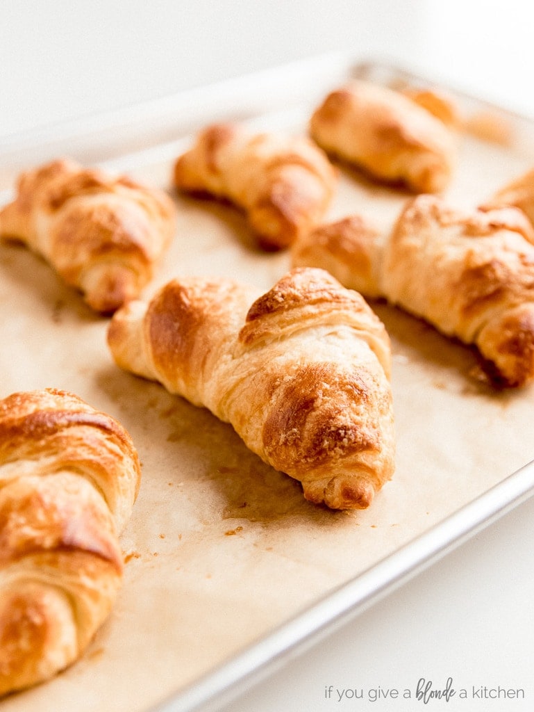 baked croissants on parchment lined baking sheet. Front croissant golden brown with flaky layers