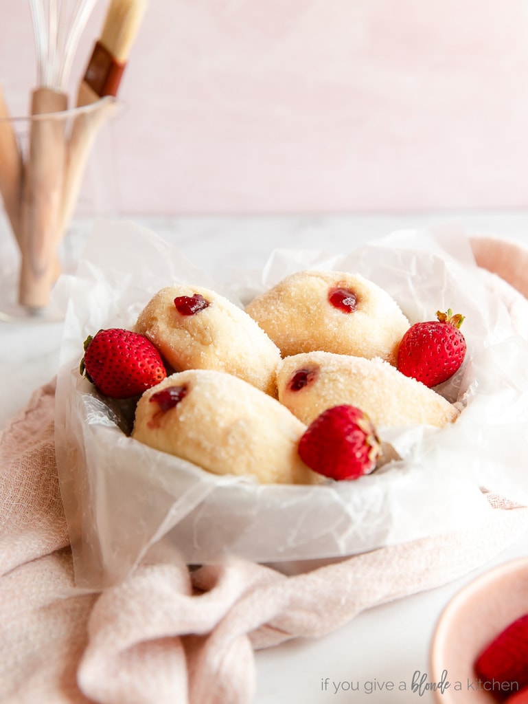 four jelly filled donuts on parchment paper in round pan with fresh strawberries