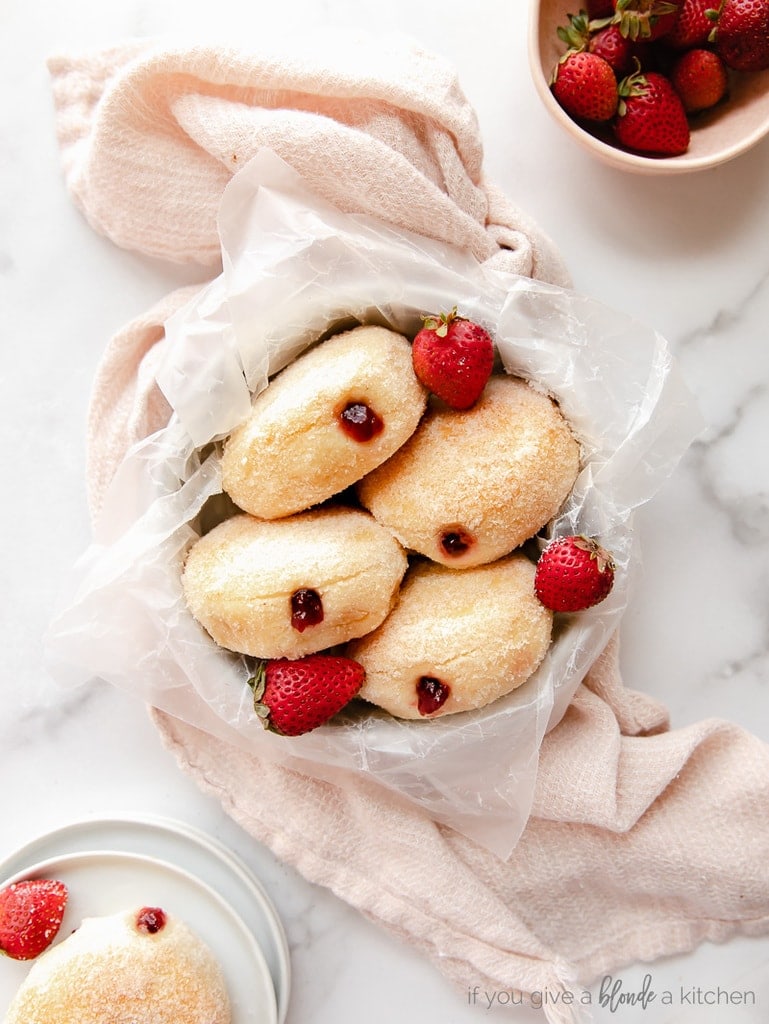four jelly filled donuts in round pan with strawberries; pan on top of pink dish cloth