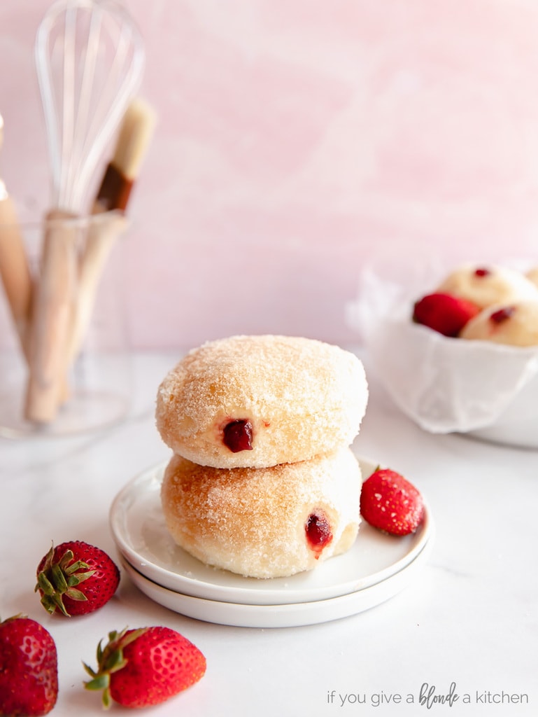 two jelly filled donuts stack o top of each other with fresh strawberries next to them