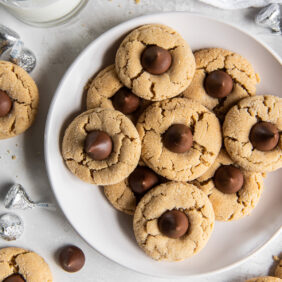 plate of peanut butter blossoms with chocolate kisses next to unwrapped kisses and glass of milk.