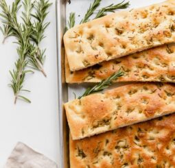 focaccia bread cut into long rectangle strips on baking pan; rosemary sprigs next to pan