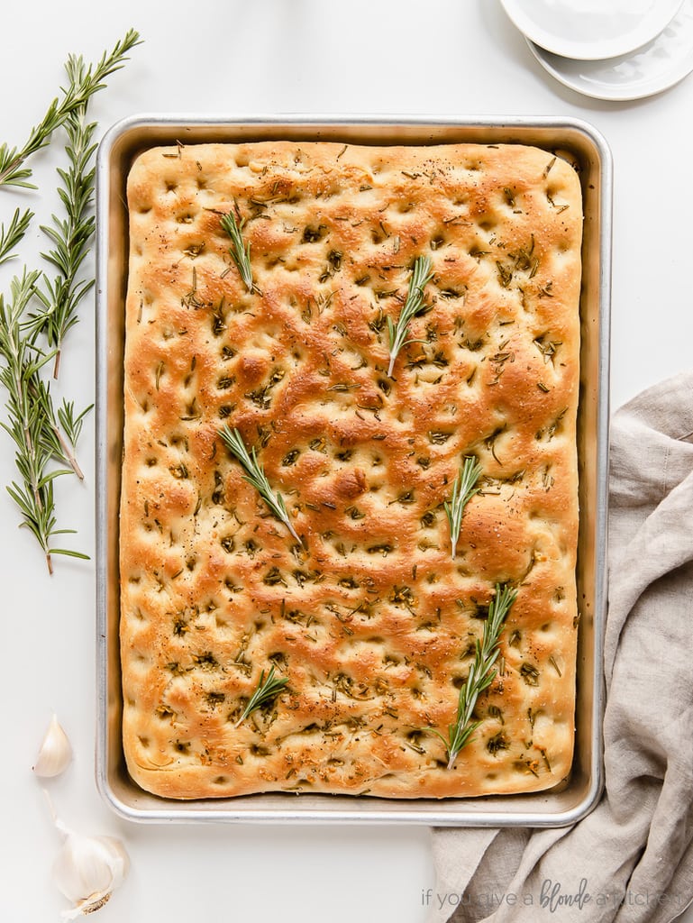 uncut focaccia bread on baking pan with fresh rosemary sprigs