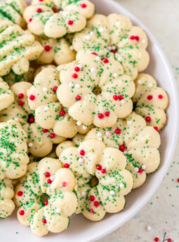 almond spritz cookies decorated with green sugar sprinkles and red nonpareils on white plate.