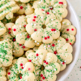 almond spritz cookies decorated with green sugar sprinkles and red nonpareils on white plate.