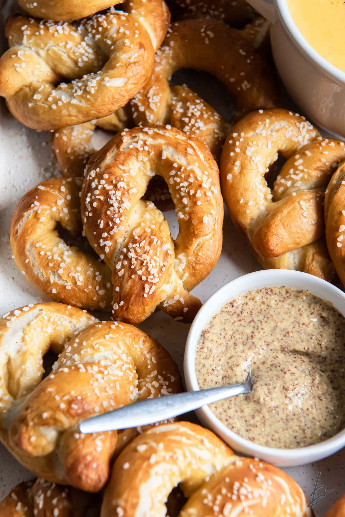 soft pretzels with salts next to white bowl of mustard with spoon.