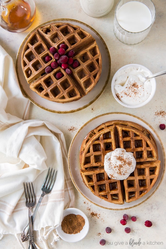 two plates of gingerbread waffles; one stack with cranberries; one stack with eggnog whipped cream