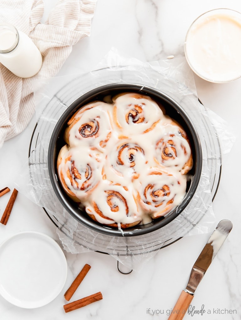 cinnamon rolls with cream cheese icing in round cake pan on round wire rack