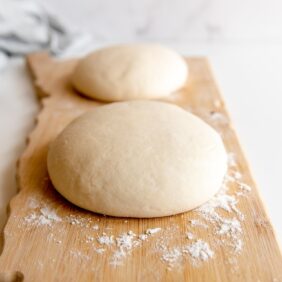 two pizza dough balls on floured wooden board