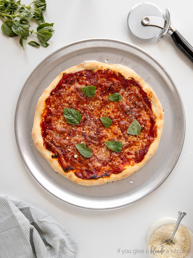 baked cheese pizza with fresh basil leaves on top of metal pizza pan