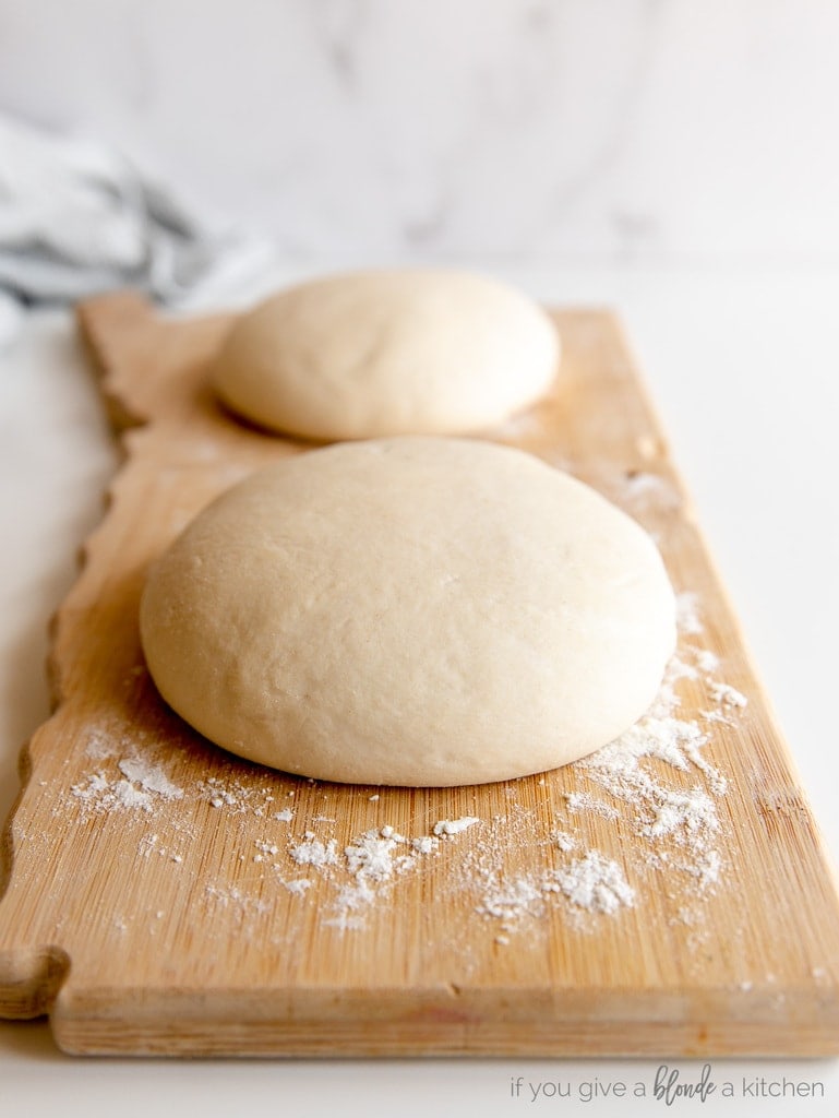 two pizza dough balls on floured wooden board