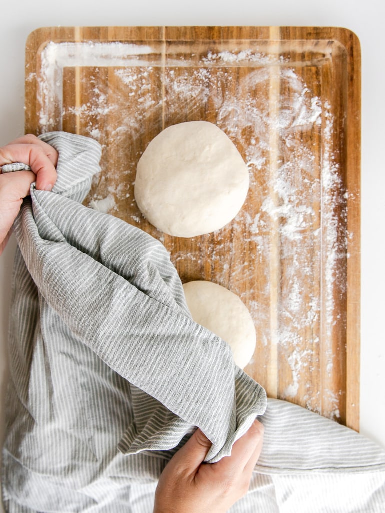 Hands draping damp kitchen cloth over pizza dough to rise