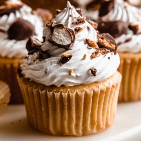 cupcakes topped with white frosting and crushed chocolate candies on marble surface