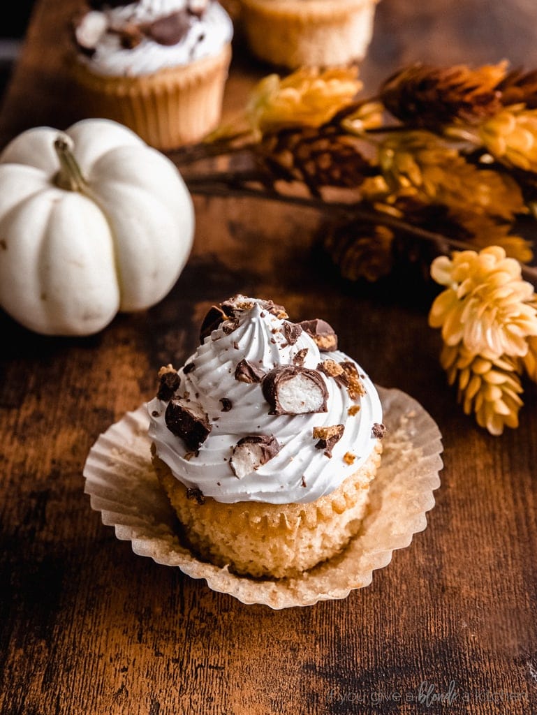 maple cupcake with marshmallow frosting and candy bits; cupcake on unfolded paper liner and dark wood surface