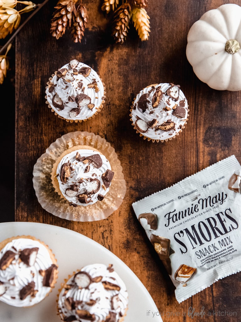 cupcakes with white frosting and candy bits on top; dark wood background with leaves and white pumpkin