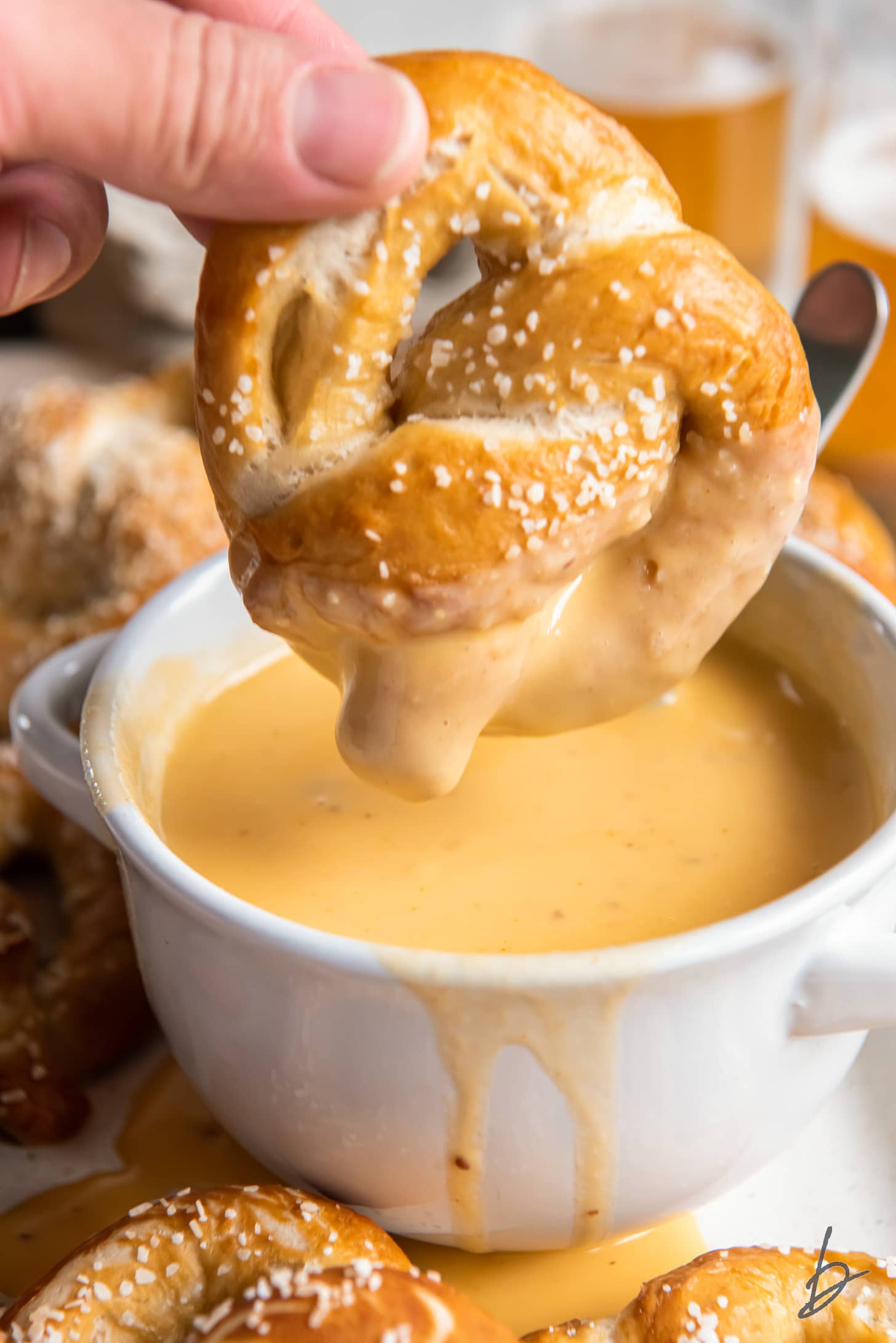 hand holding soft pretzel and dipping it in beer cheese dip.