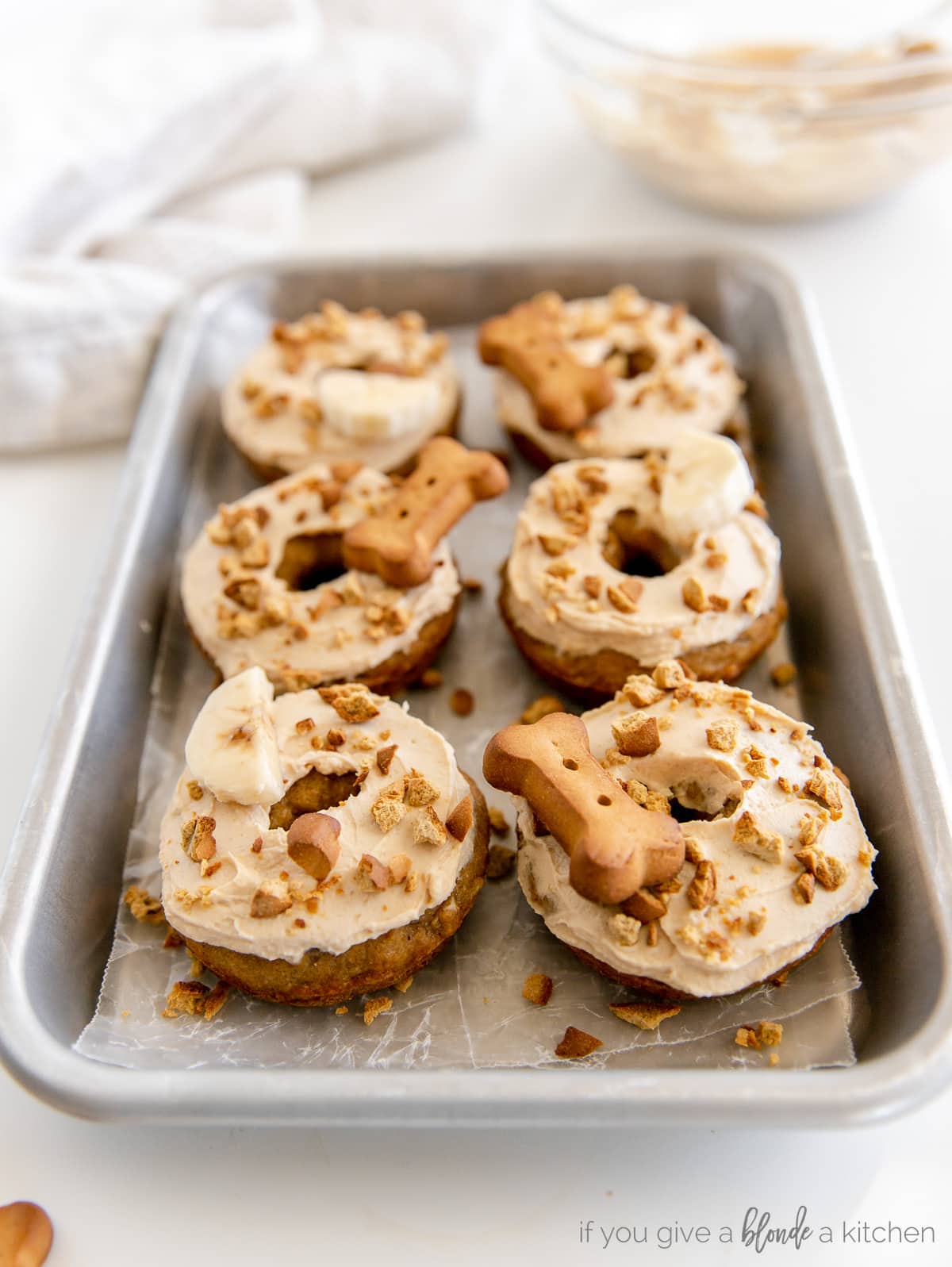 dog donuts topped with frosting and crushed dog biscuits on baking sheet