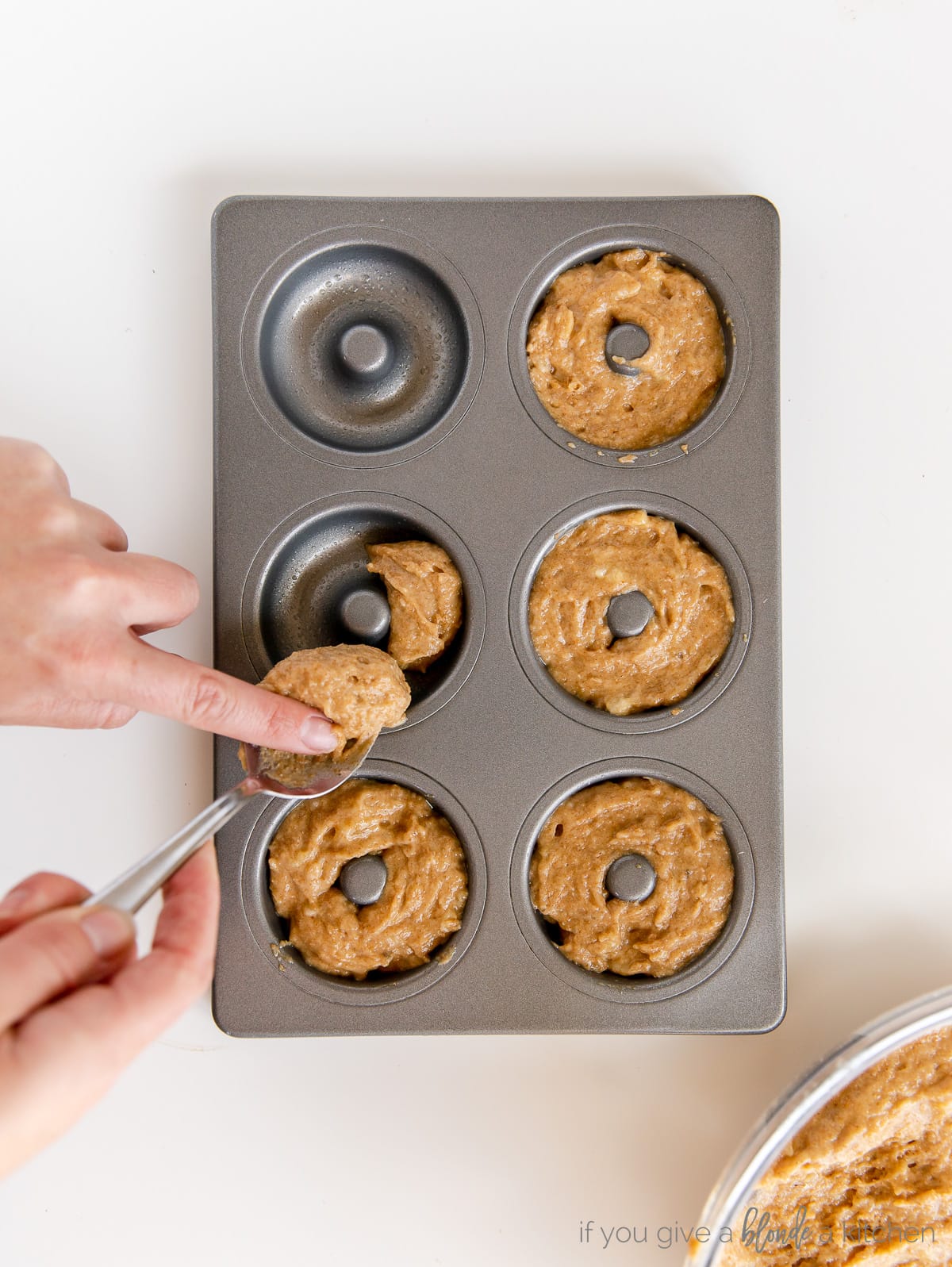 hand transferring donut batter from spoon to donut pan