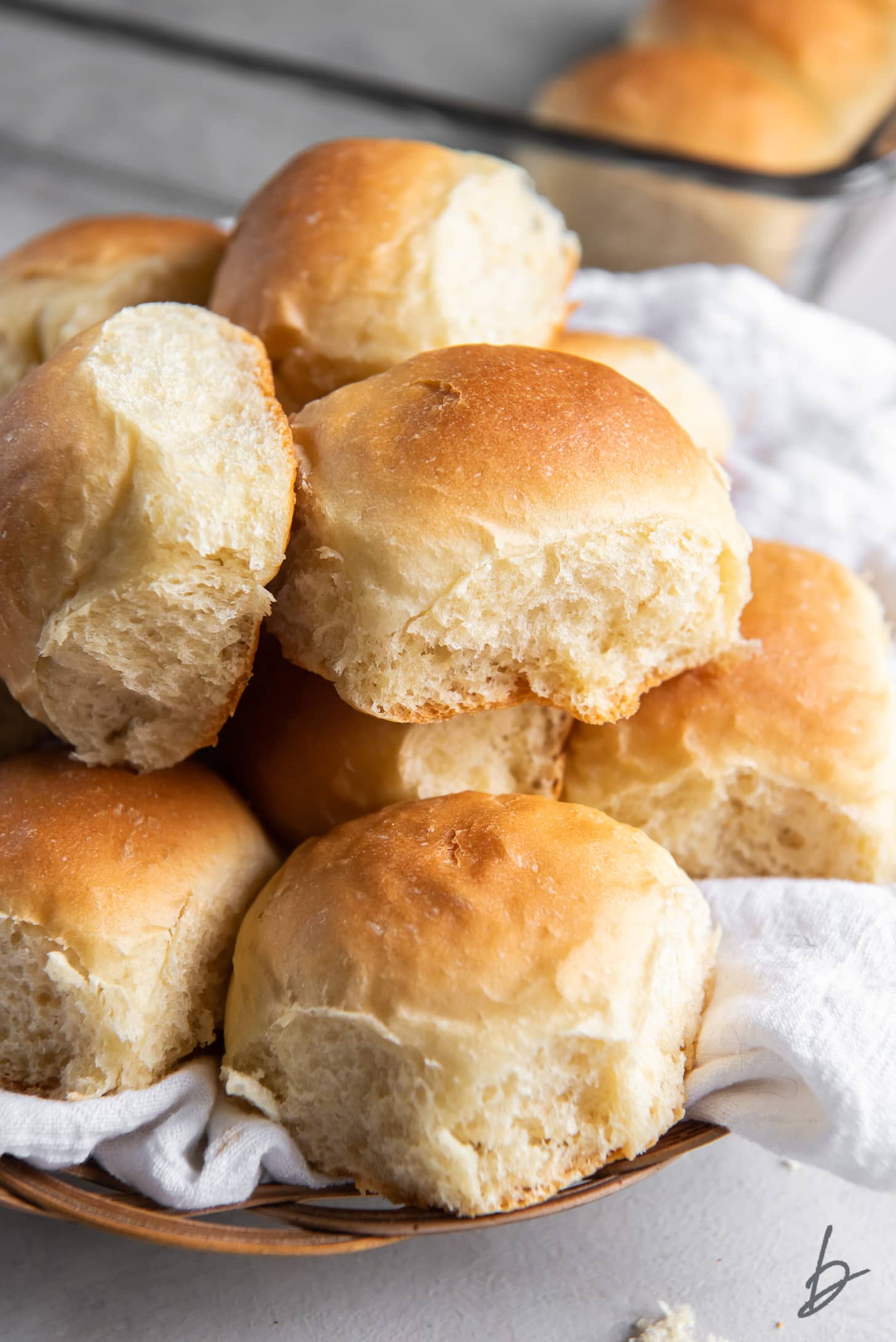 fluffy homemade dinner rolls in a pile on white cloth in basket