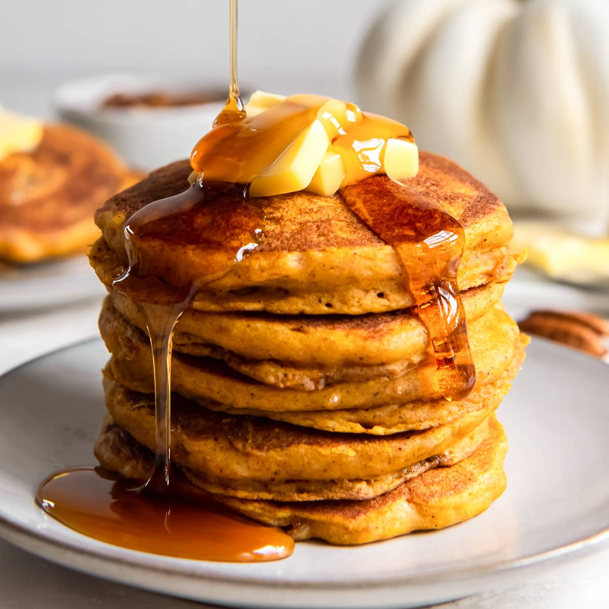 stack of pumpkin pancakes with syrup being poured over it.