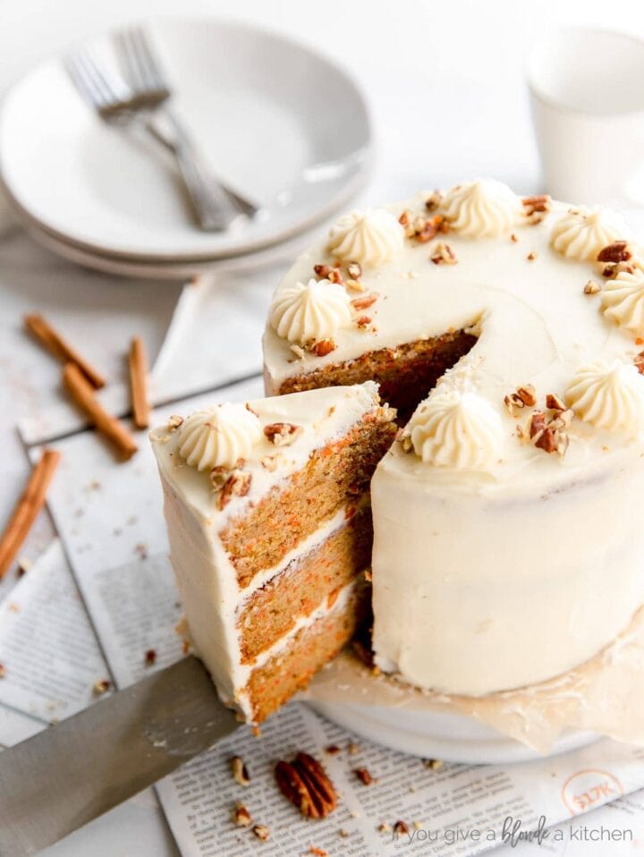cake server taking slice of three layer carrot cake out of round cake with cream cheese frosting