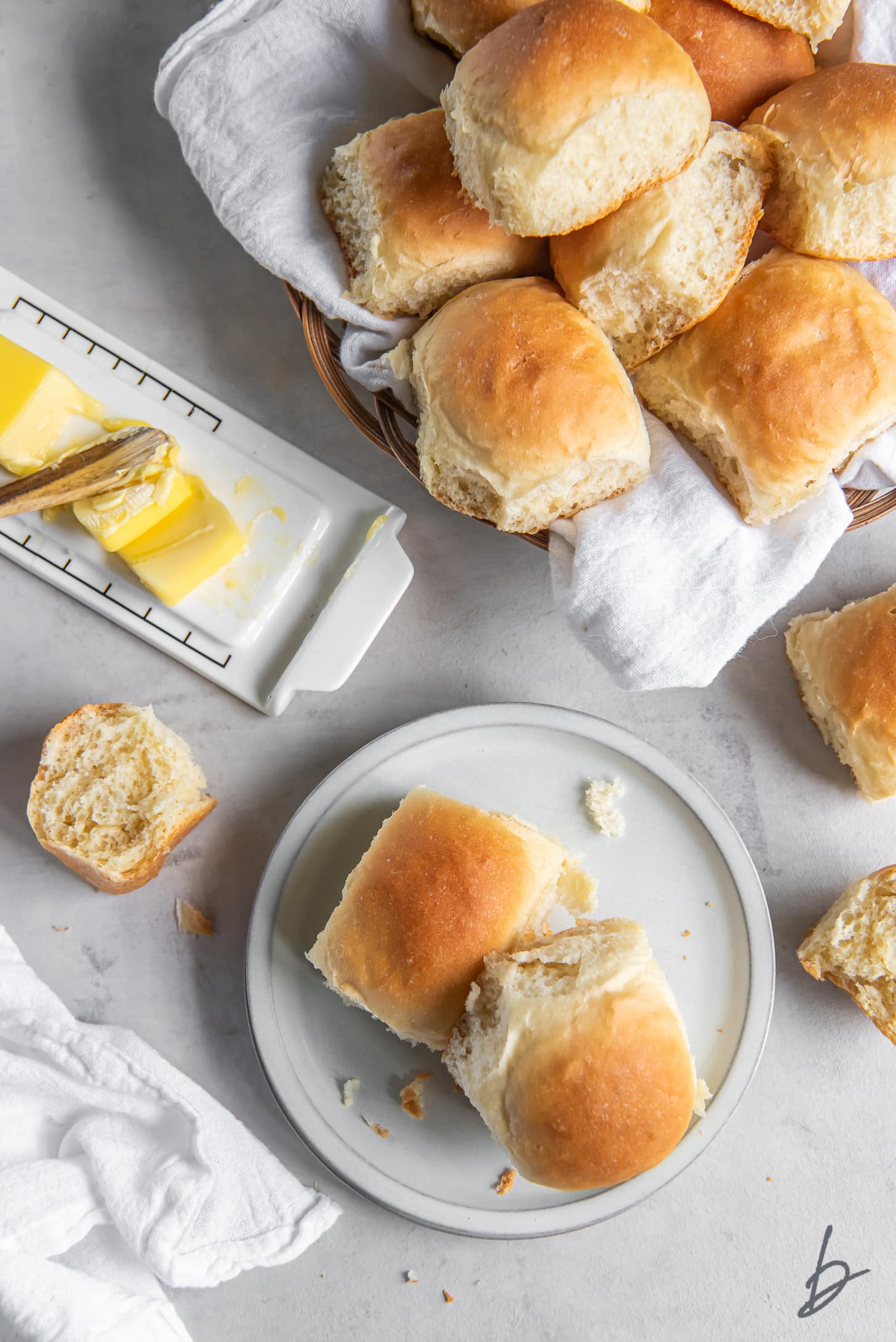 two homemade dinner rolls on a plate next to basket of rolls and butter stick
