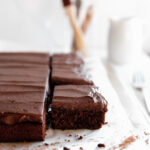 square slice of chocolate sheet cake next to rest of cake with chocolate buttercream frosting