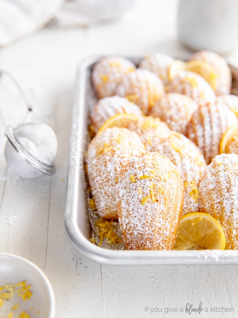 madeleine cookie leaned up against more madeleines layered in baking sheet.