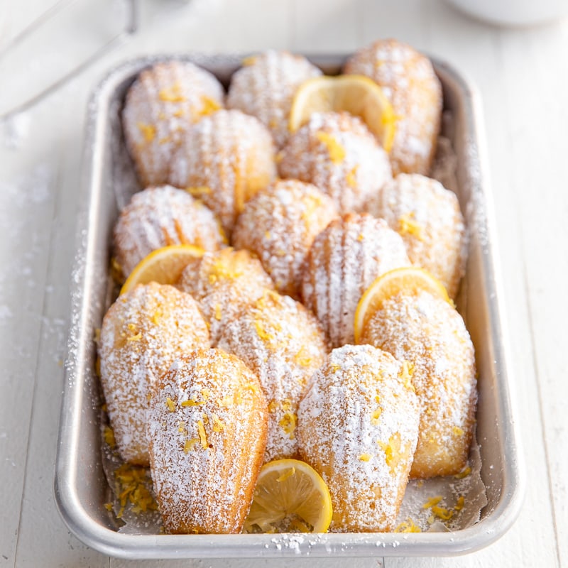 rectangular baking sheet with madeleines dusted in confectioners' sugar leaned up against each other