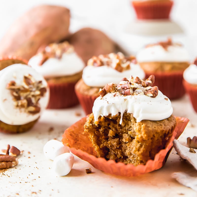 bite taken out of a sweet potato cupcakes with marshmallow frosting sitting on orange paper liner