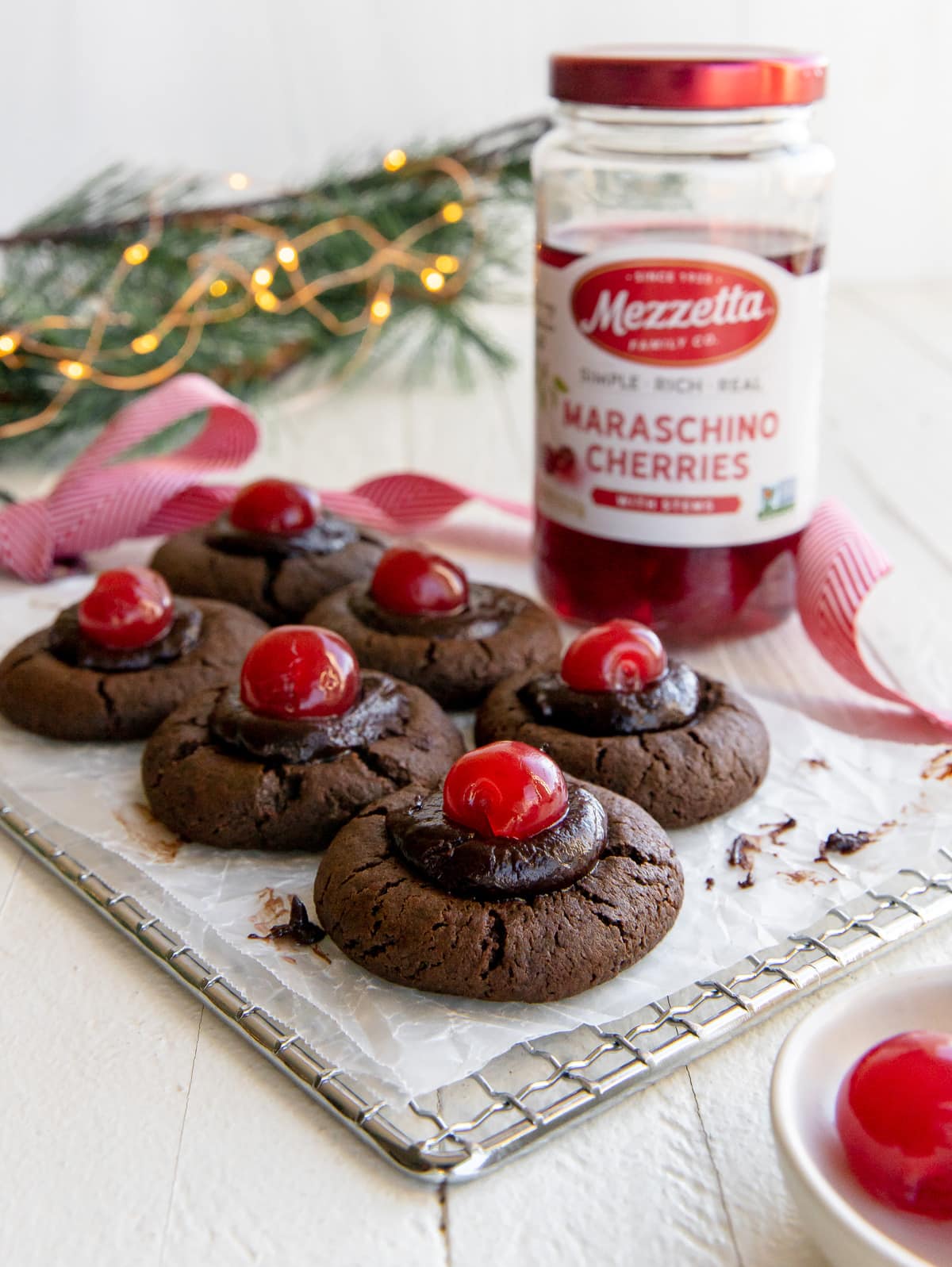 chocolate cherry thumbprint cookies on wire cooling rack; jar of maraschino cherries next to cookies