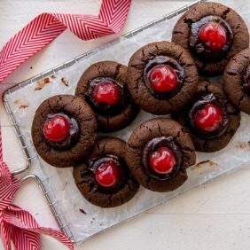 hand reaching for chocolate cherry thumbprint cookie on wire cooling rack with handle tied with ribbon