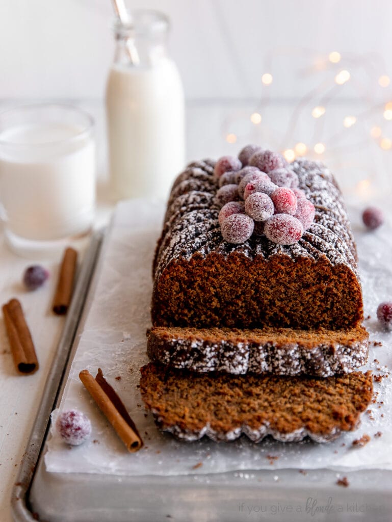 gingerbread loaf with two slices cut off the end; loaf topped with sugared cranberries and confectioners' sugar