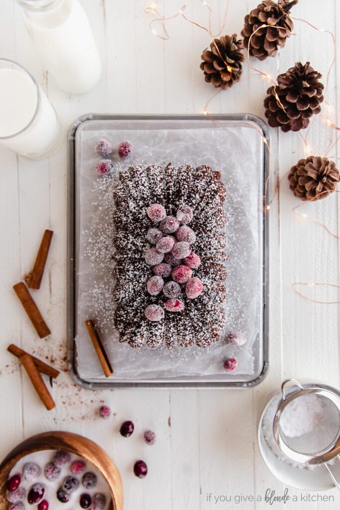 gingerbread loaf dusted with confectioners sugar and topped with sugared cranberries on baking sheet