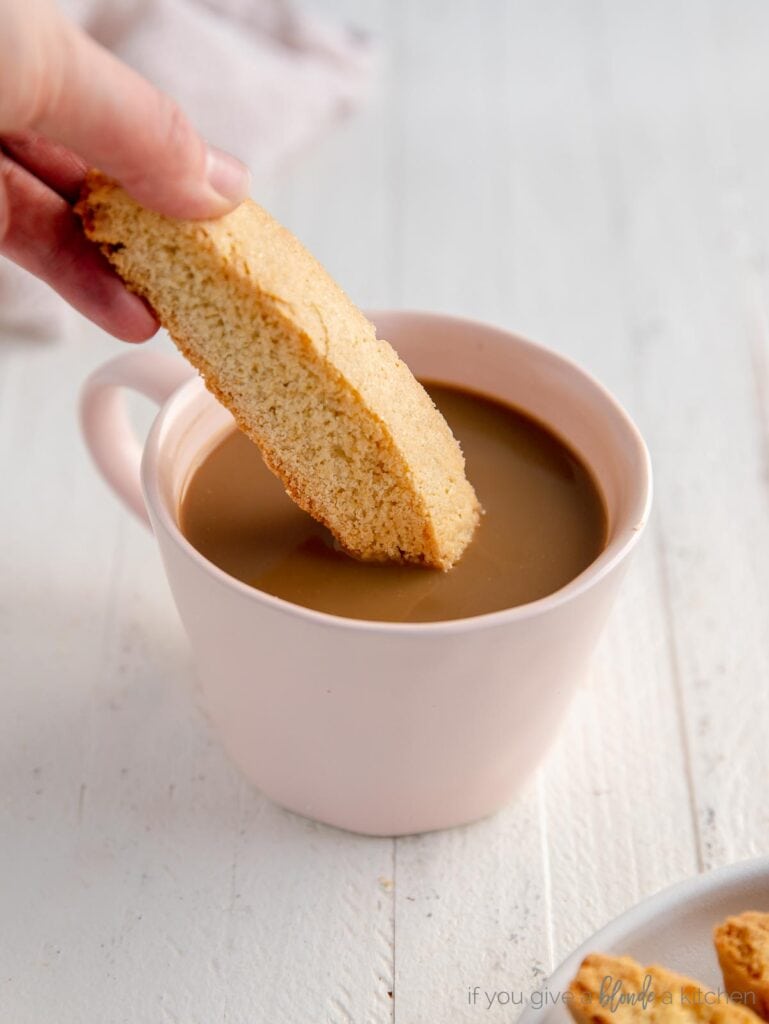 hand dipping biscotti in pink mug of coffee