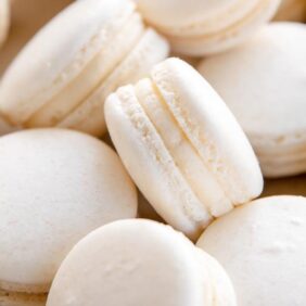 white macaron with buttercream filling leaning on its side on top of other macarons