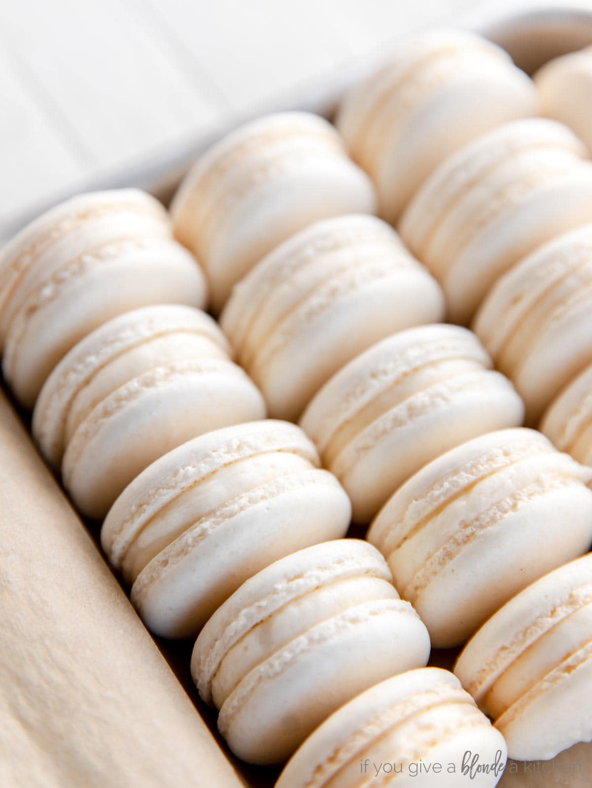 macarons with buttercream filling lined up in rows on a baking sheet
