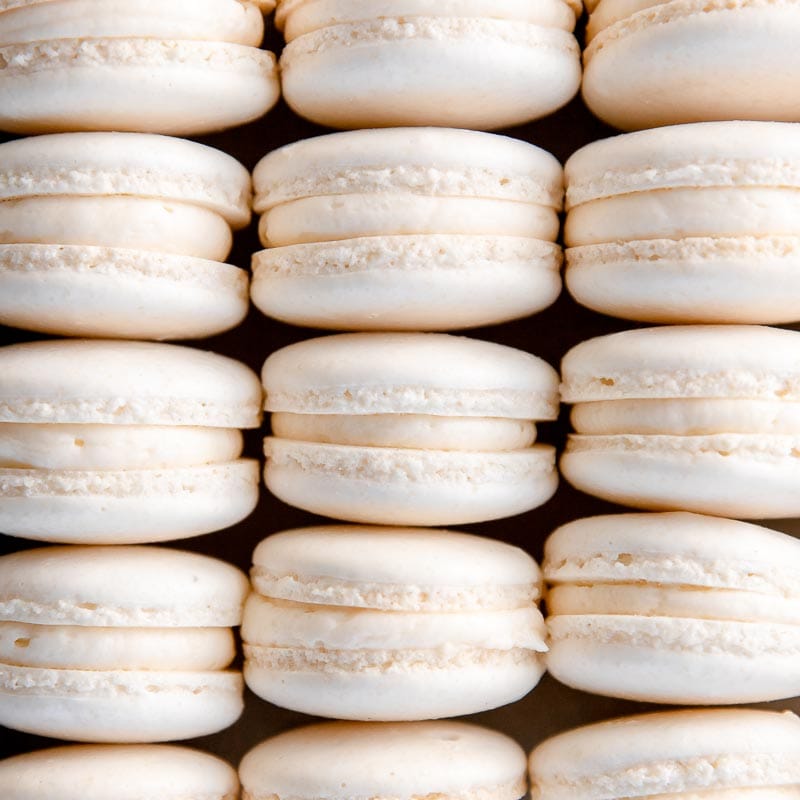 white macarons in rows showing macaron feet and buttercream filling inside