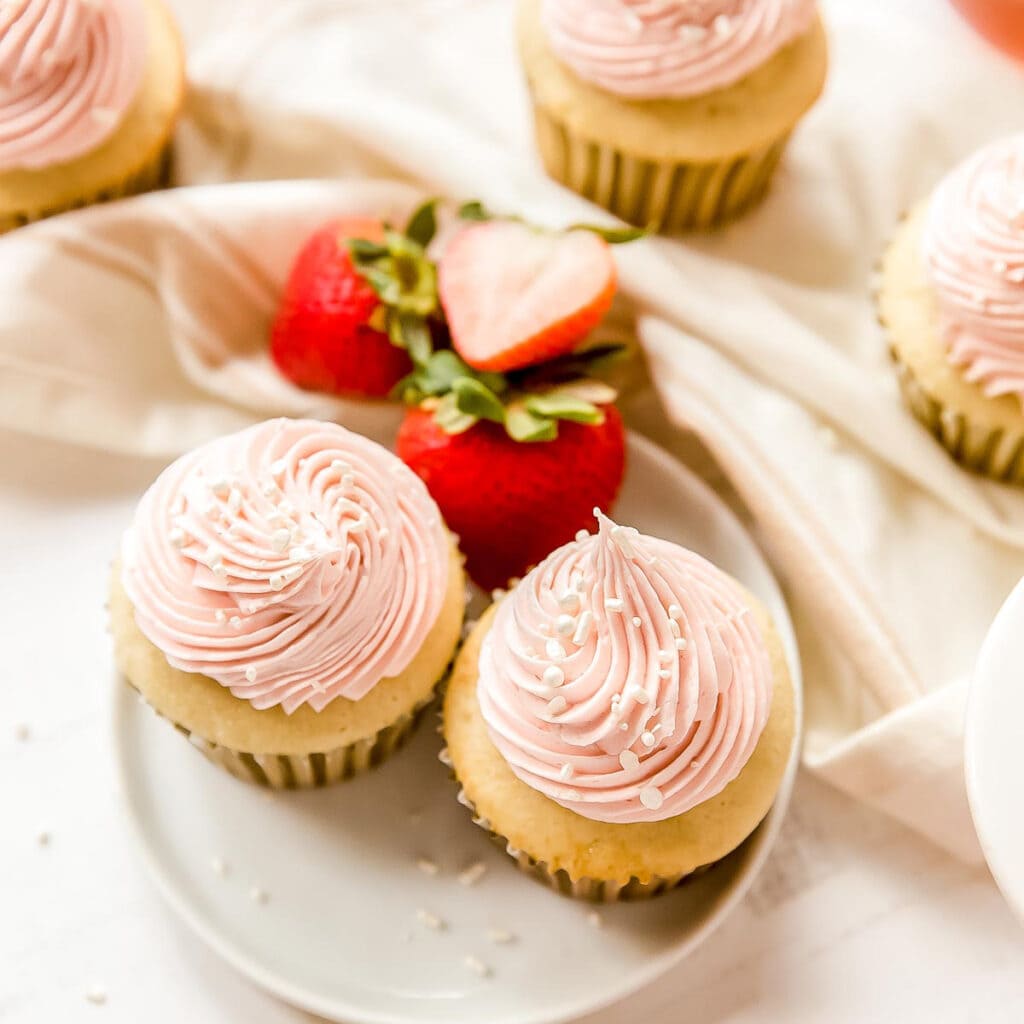 two moscato cupcakes with pink frosting on a plate with strawberries