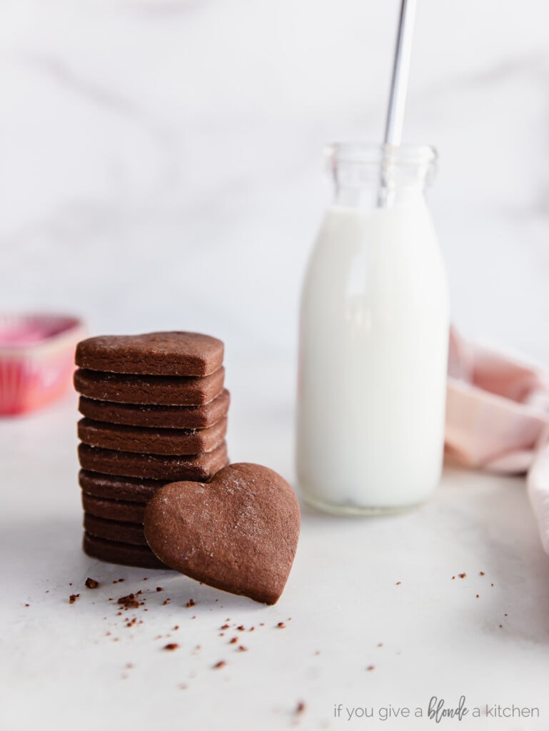 stack of chocolate cut out cookies next to glass jar of milk