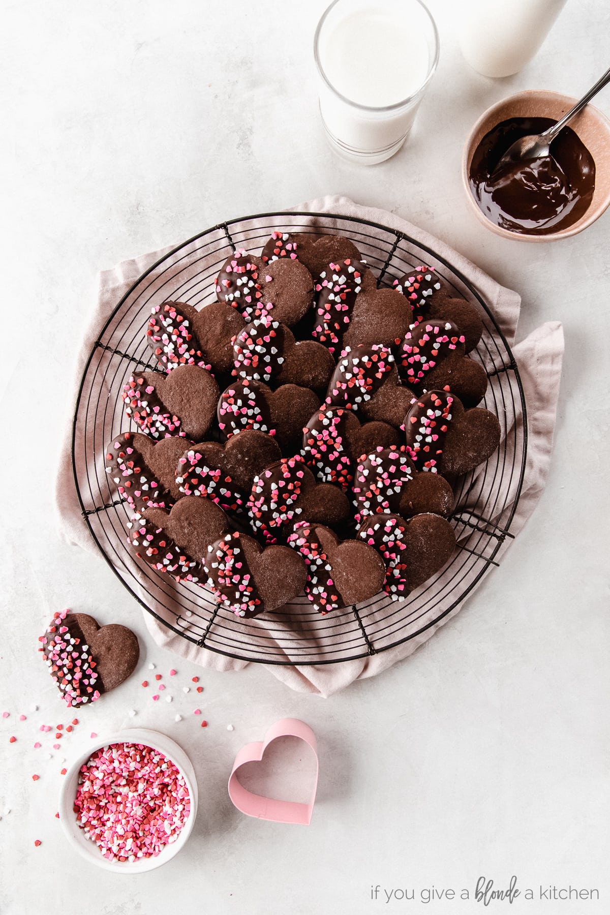 chocolate heart cookies with melted chocolate and red and pink sprinkles on round wire cooling rack
