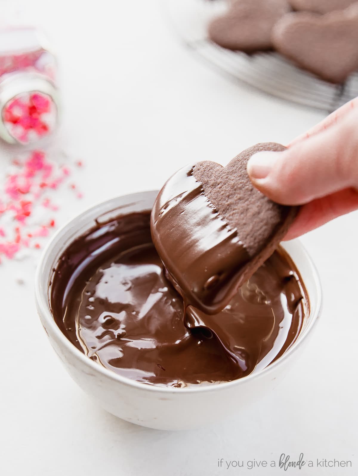 heart shaped chocolate cookie being dipped in a bowl of melted chocolate