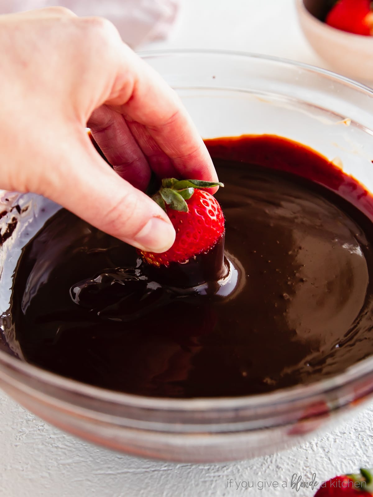 hand dipping strawberry in bowl of chocolate ganache
