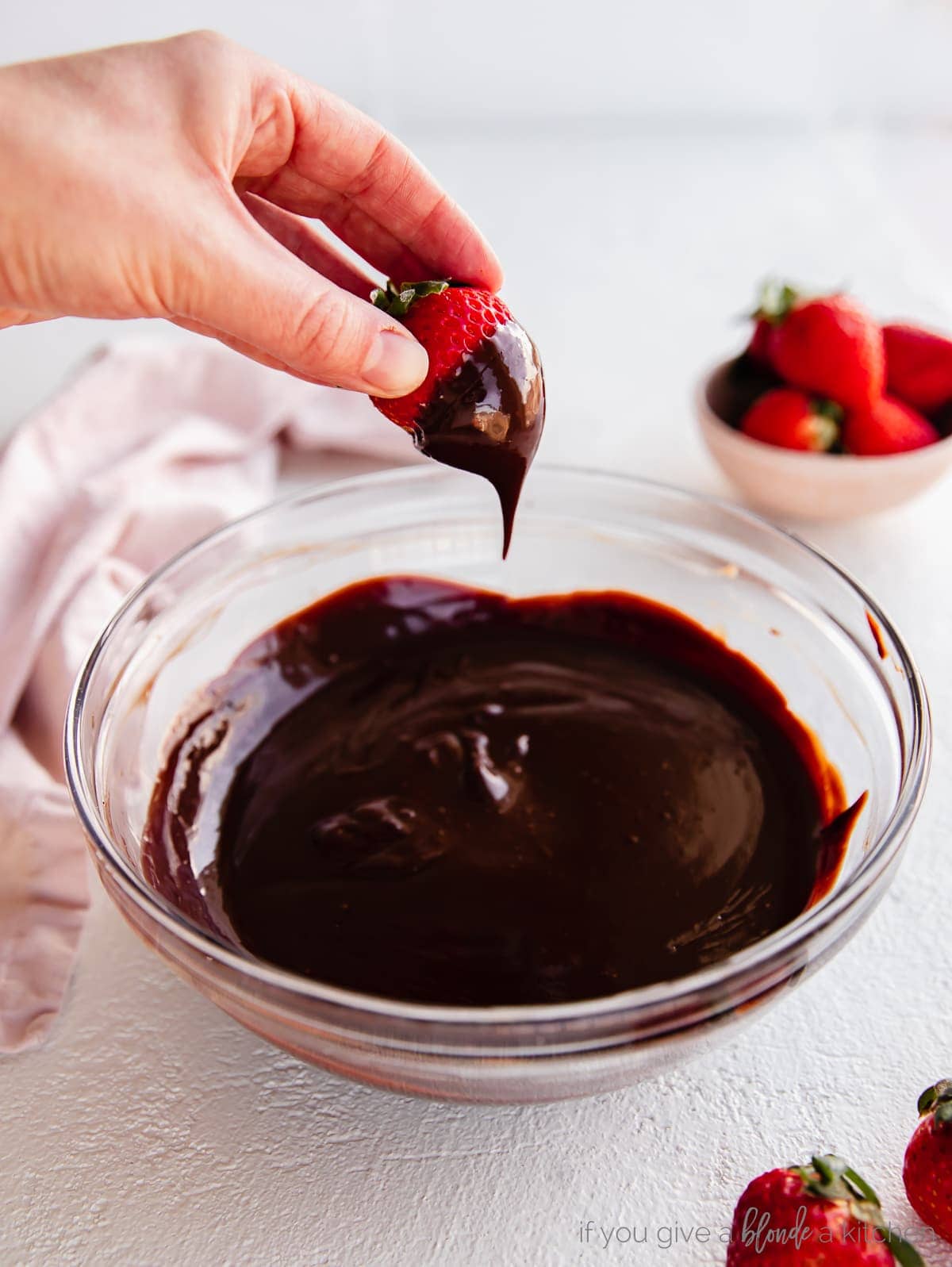 hand holding strawberru covered in chocolate ganache of bowl of chocolate ganache
